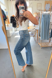Person wearing a white top and blue jeans taking a mirror selfie in a clothing store.