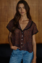 Load image into Gallery viewer, Woman wearing a patterned blouse and jeans against a wooden background