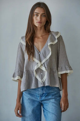 Woman wearing a striped blouse with ruffled details and blue jeans against a plain background