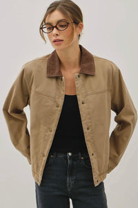 Woman wearing a beige jacket over a black top and jeans on a plain background
