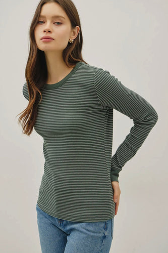 Woman wearing a green striped long-sleeve shirt and blue jeans against a plain background