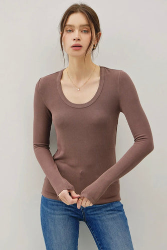 Woman wearing a brown long-sleeve top and blue jeans against a plain background