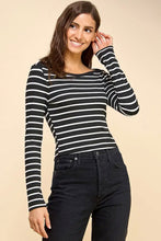 Load image into Gallery viewer, A woman modeling a black and white horizontally striped long-sleeve boat-neck top, paired with dark jeans, against a solid beige studio background.