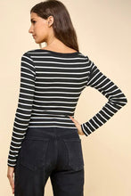 Load image into Gallery viewer, A woman shown from the back wearing a black and white horizontally striped long-sleeve top and dark jeans, standing against a solid beige studio background.