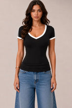 Load image into Gallery viewer, A woman modeling a black short-sleeve V-neck t-shirt with white contrast trim on the collar and sleeve cuffs, paired with blue jeans, against a solid light beige background.