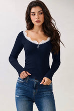 Load image into Gallery viewer, A woman modeling a navy blue long-sleeve top with a white lace-trimmed scoop neckline and three small decorative buttons at the center chest, paired with blue jeans against a plain light background.