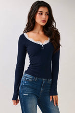 Load image into Gallery viewer, A woman modeling a navy blue long-sleeve top with a white lace-trimmed scoop neckline and small button details, paired with blue jeans, against a light gray studio background.