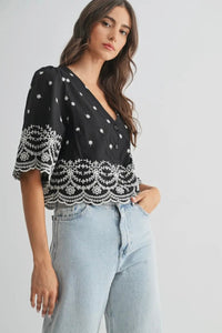 Woman wearing a black top with white lace details and light blue jeans on a gray background