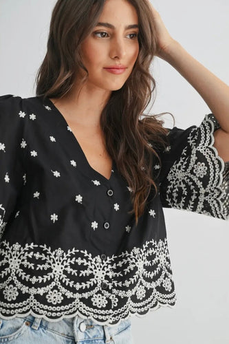 Woman wearing a black blouse with white floral patterns on a plain background