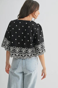 Black top with white lace details worn by a person on a plain background