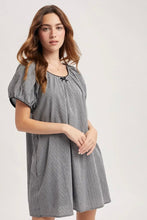 Load image into Gallery viewer, A woman modeling a short-sleeve, knee-length dress with a small-scale black and white gingham pattern, puff sleeves, and a gathered neckline.