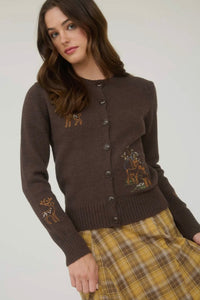 Woman wearing a brown cardigan with embroidered details on a plain background