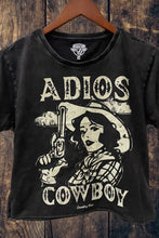 Load image into Gallery viewer, Black t-shirt with graphic design of a woman in a cowboy hat holding a gun, text 'Adios Cowboy', on a wooden background.