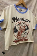 Load image into Gallery viewer, T-shirt with 'Montana Big Sky Country' graphic on a hanger against a textured wall.