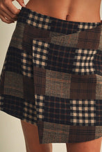 Load image into Gallery viewer, A close-up of a patchwork plaid skirt worn by a model, featuring blocks of navy, brown, and beige tartan and gingham patterns.