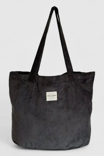 Black corduroy tote bag with a visible brand label on a light gray background