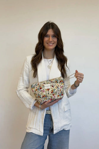 Woman holding a floral clutch against a plain background