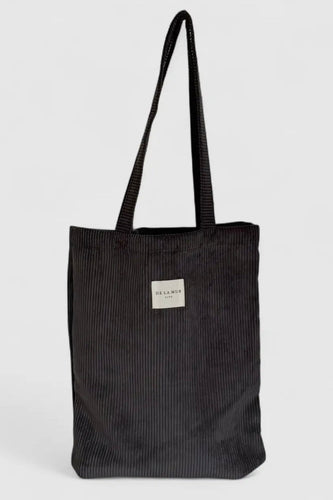 Black corduroy tote bag with a visible brand label on a light gray background