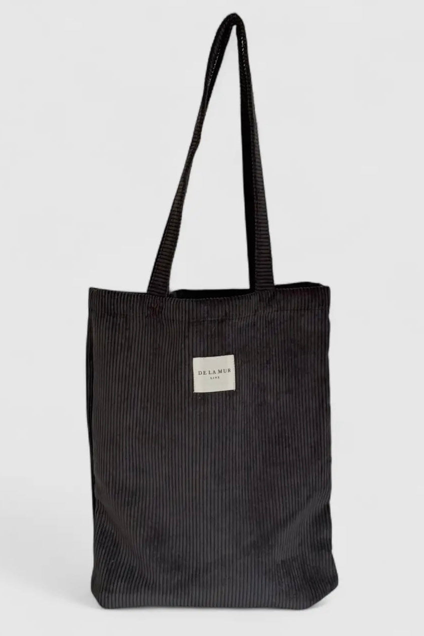 Black corduroy tote bag with a visible brand label on a light gray background