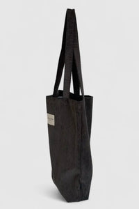 Black tote bag with a visible brand label on a light gray background