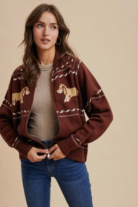Woman wearing a brown patterned cardigan over a gray sweater with blue jeans on a beige background