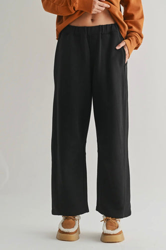 Person wearing black wide-leg pants and a brown sweater on a light gray background