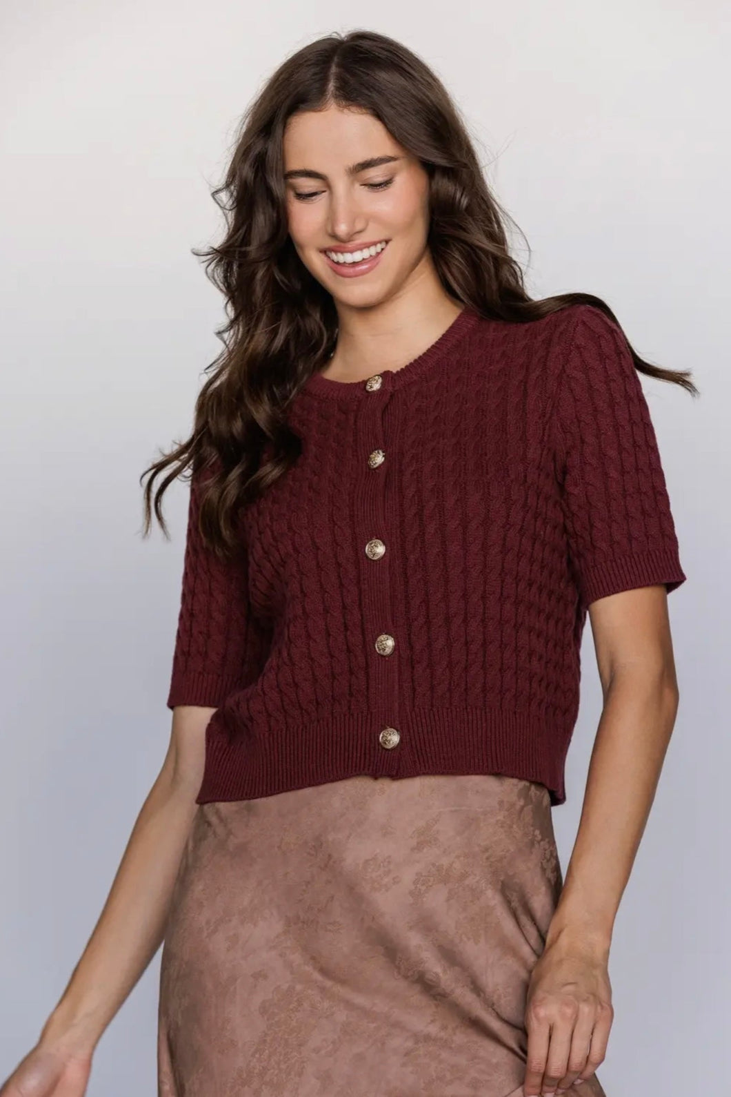 Woman wearing a maroon knitted cardigan against a plain background