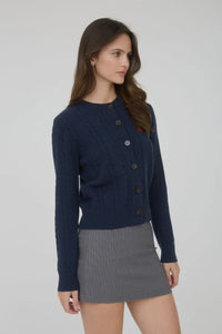 Woman wearing a navy blue ribbed sweater and gray skirt on a plain background
