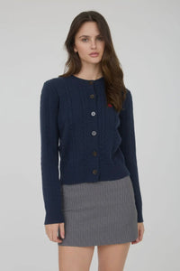 Woman wearing a navy blue cardigan and gray skirt on a plain background