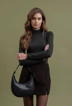 Load image into Gallery viewer, Woman holding a black handbag against a green background