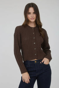 Woman wearing a brown ribbed sweater and dark jeans on a plain background