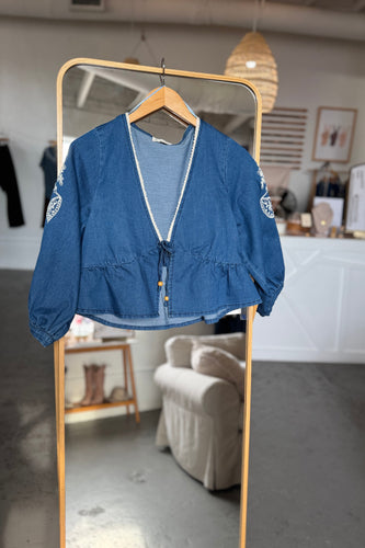 Blue denim jacket on a hanger in front of a mirror in a room.