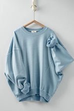 Load image into Gallery viewer, A light blue crewneck sweatshirt with a unique gathered sleeve detail, hanging on a wooden hanger against a plain light gray wall.
