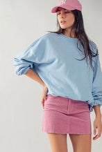 Load image into Gallery viewer, A woman wearing a light blue oversized crewneck sweatshirt, a pink denim mini skirt, and a pink baseball cap with a white NY logo, posing against a light gray studio background.