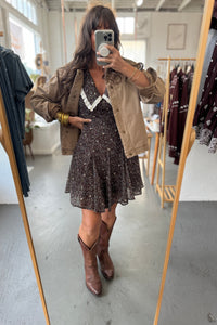 Person taking a mirror selfie wearing a dress and jacket in a clothing store.