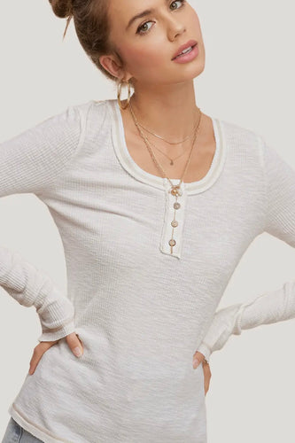 Woman wearing a light gray long-sleeve top with buttons on a plain background