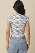 Load image into Gallery viewer, Person wearing a white t-shirt with blue floral pattern and light blue jeans on a beige background