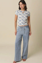 Load image into Gallery viewer, Woman wearing a floral top and light blue pants on a beige background