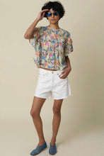 Load image into Gallery viewer, Person wearing a floral top and white shorts with sunglasses on a beige background
