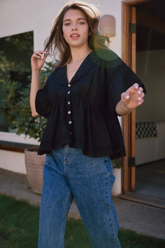 Woman wearing a black blouse and blue jeans outdoors.