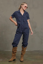 Load image into Gallery viewer, Woman wearing a navy blue jumpsuit and brown boots against a gray background