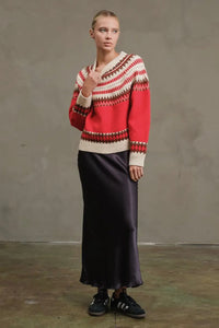 Person wearing a patterned sweater and dark skirt against a plain background