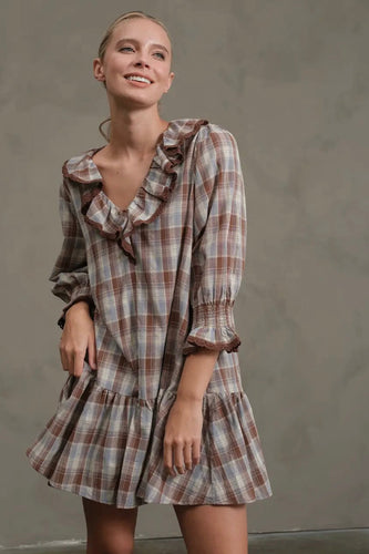 Woman wearing a plaid dress with ruffled details against a plain background