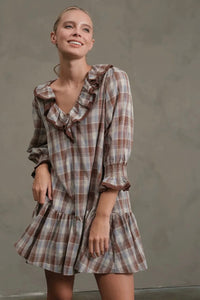 Woman wearing a plaid dress with ruffled details against a plain background