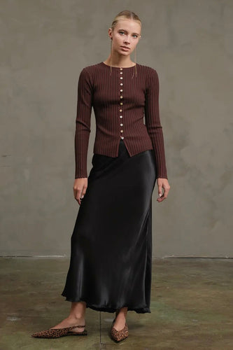 Woman wearing a brown ribbed sweater and black satin skirt against a plain background