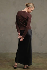 Woman wearing a brown sweater and black skirt against a plain background
