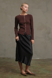 Woman wearing a brown ribbed sweater and black skirt against a plain background