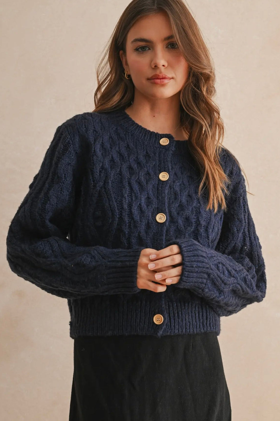 Woman wearing a navy blue knitted cardigan with gold buttons on a beige background