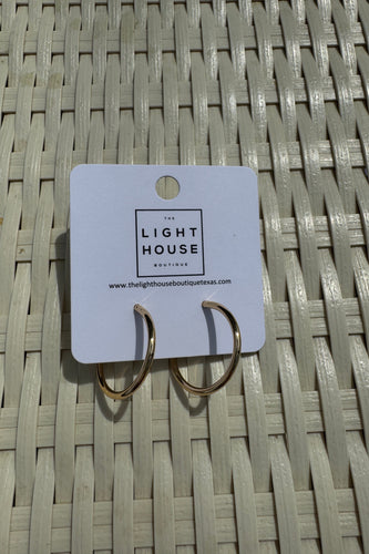 Gold earring on a Lighthouse brand card against a woven mat background
