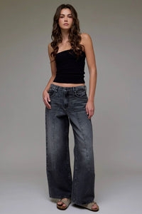 Woman wearing a black top and wide-leg jeans against a neutral background